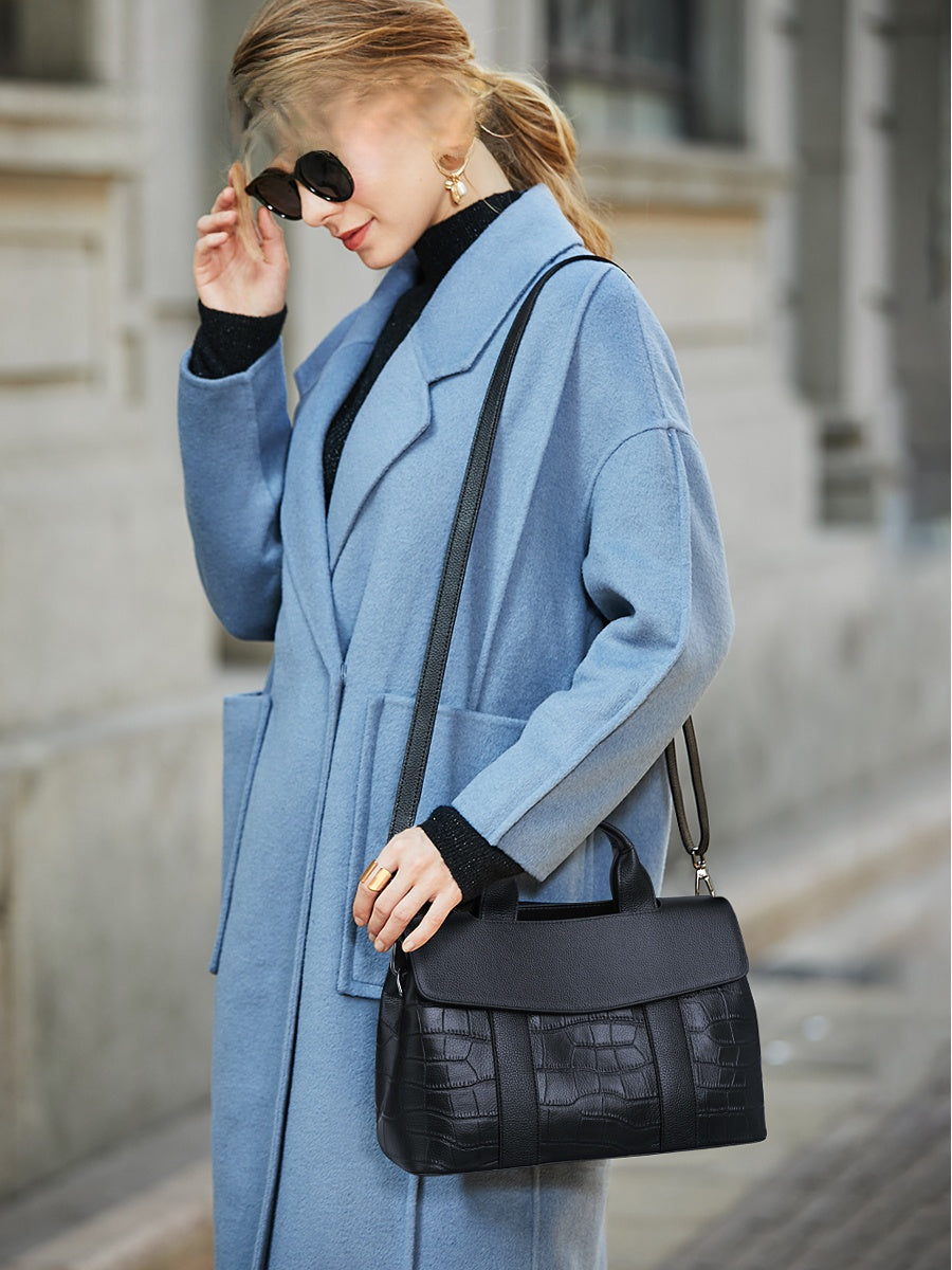 Woman in a blue coat holding a black handbag on a city street.